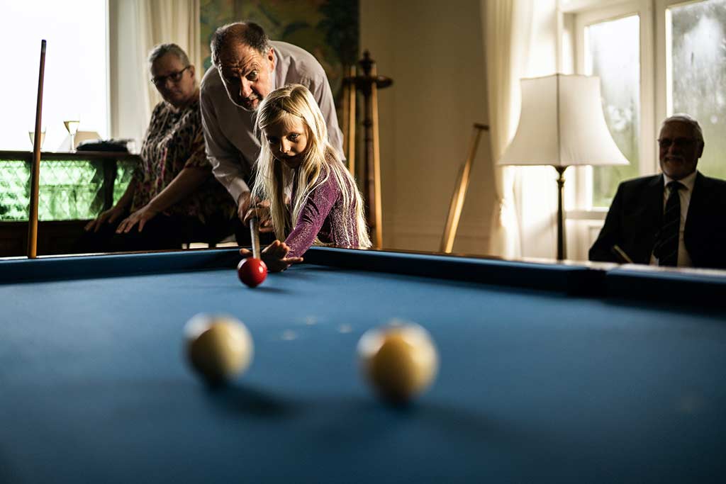 elderly man teaching young girl how to play snooker
